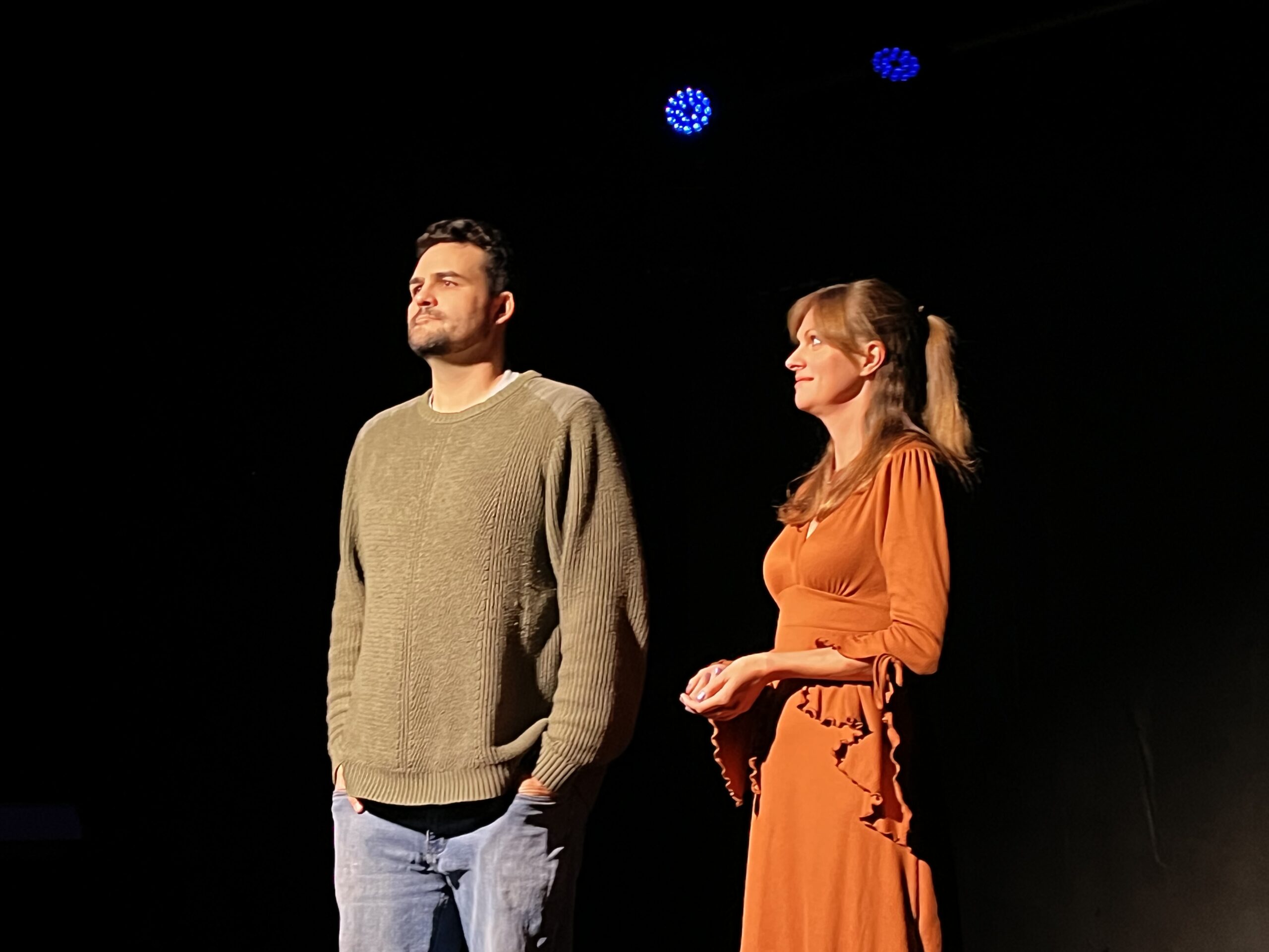 Man and woman standing on stage in spotlight.